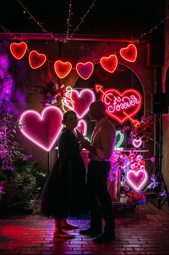 a bright neon heart wedding backdrop with a garland, colorful hearts and some blooms is amazing for a dance floor