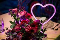 a bright wedding centerpiece of red and fuchsia blooms and greenery plus a pink neon heart sign is amazing