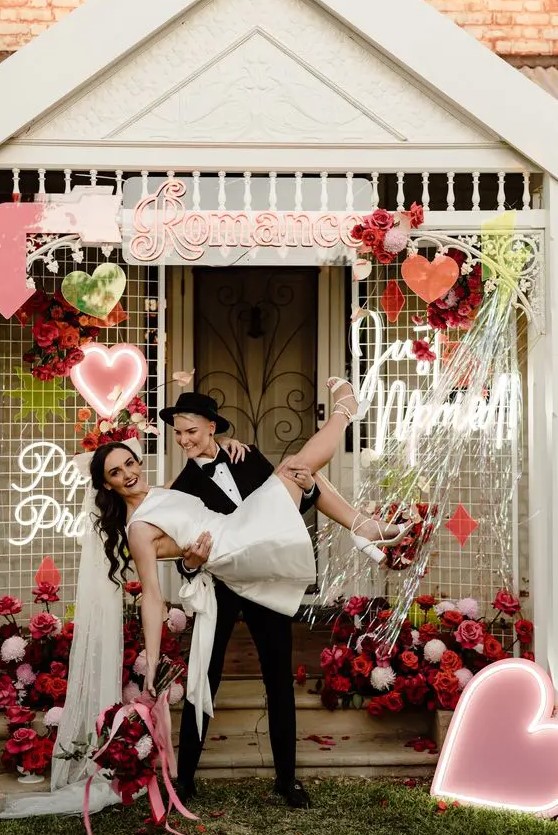 a bright wedidng backdrop with pink, red and white blooms, a neon heart and some more decor is a lovely and bright idea for a wedding