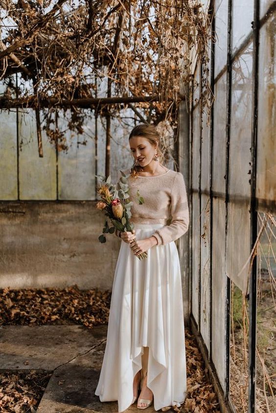 a casual bridal outfit with a tan cropped sweater, a white pleated asymmetrical skirt and shiny shoes