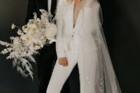a chic white pantsuit with cropped pants, sheer heels and a long veil with sequins for a comfy reception look