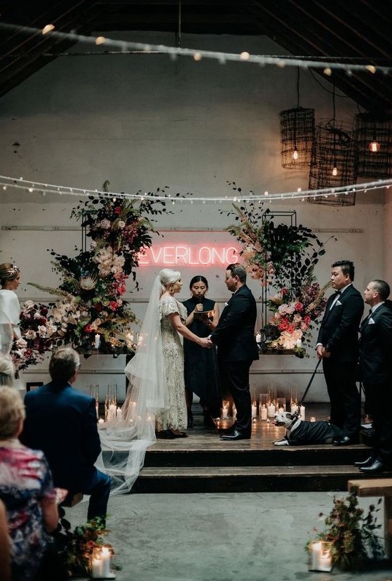 a fantastic wedding ceremony space with lots of candles, lush blooms and greenery and a neon sign