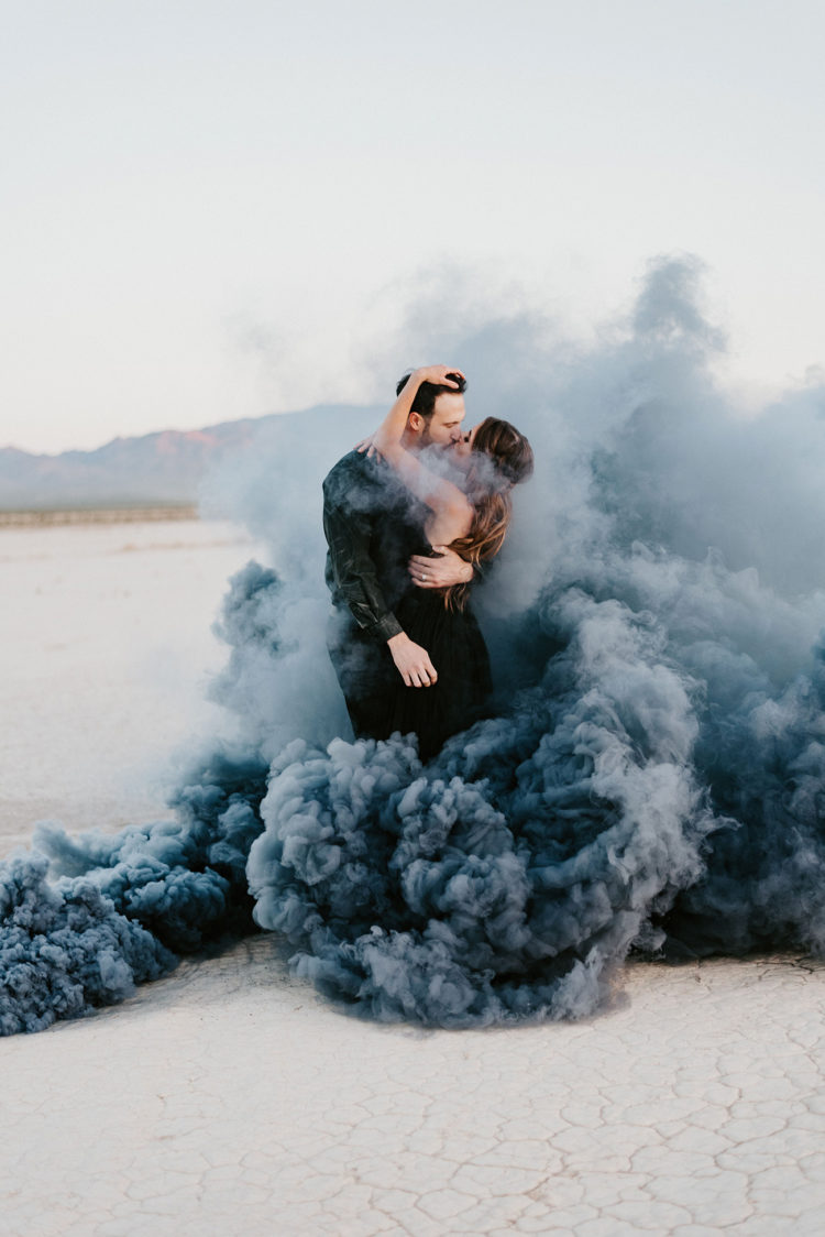 a gorgeous engagement photo of a couple in black standing in black smoke in a desert just wows