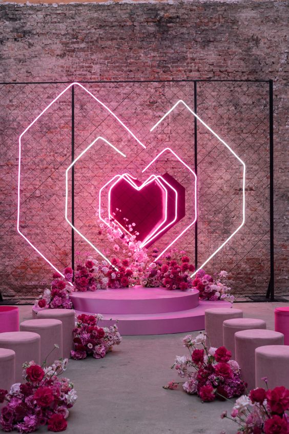 A jaw dropping wedding ceremony space with neon hearts, pink, fuchsia and blush blooms, matching floral arrangements along the aisle