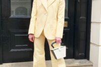a light yellow pantsuit with flare pants and no top underneath, a two-tone bag, strappy shoes and a chunky chain necklace