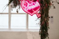 a lush greenery and bright pink blooms wedding arch with a large pink neon heart is a stunning modern idea