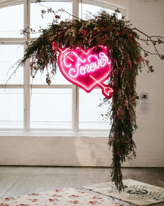 a lush greenery and bright pink blooms wedding arch with a large pink neon heart is a stunning modern idea
