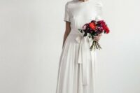 a minimalist A-line wedding dress with a high neckline, short sleeves and a pleated skirt plus a sash