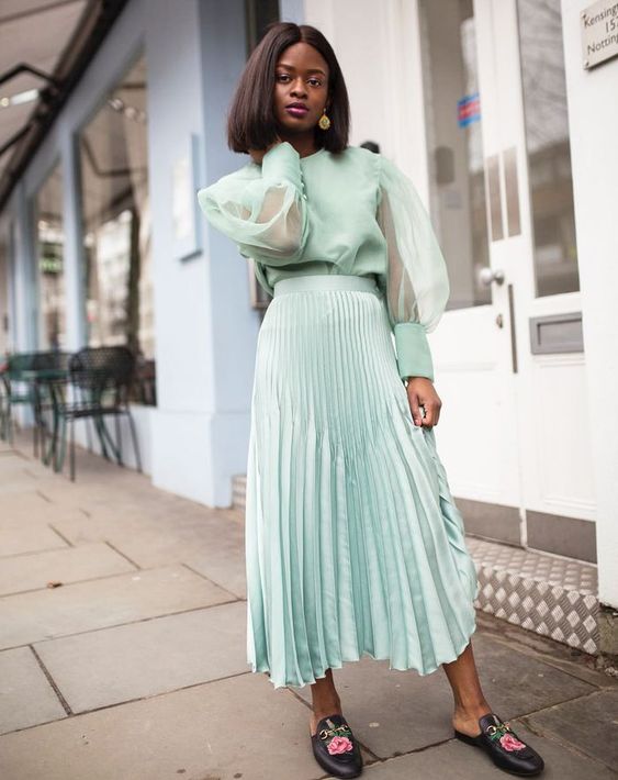 a mint-colored wedding guest outfit with a blouse with puff sleeves, a pleated midi skirt, black slippers and statement earrings