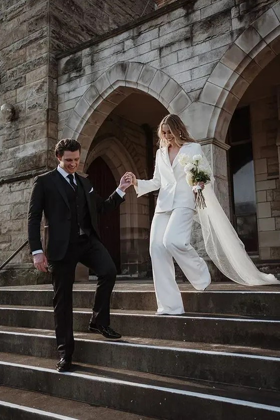 a modern bridal pantsuit with an oversized blazer and wide pants, a long veil are a lovely combo for amodern wedding