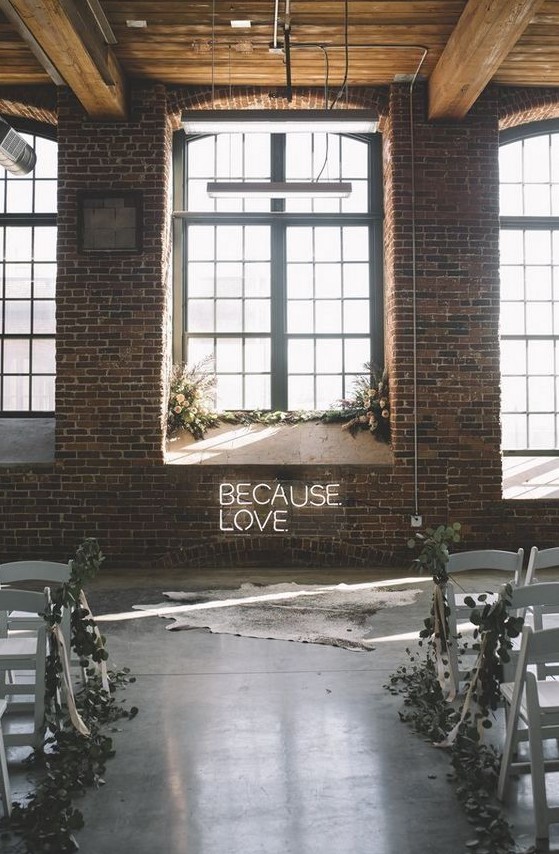 a modern industrial wedding ceremony space with a neon sign, lush floral arrangements with greenery and a faux animal skin rug