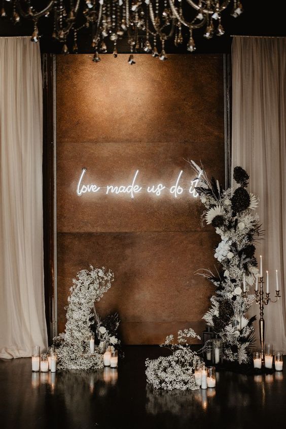 a modern wedding altar of white blooms, candles and a neon sign is a super cool and bold solution