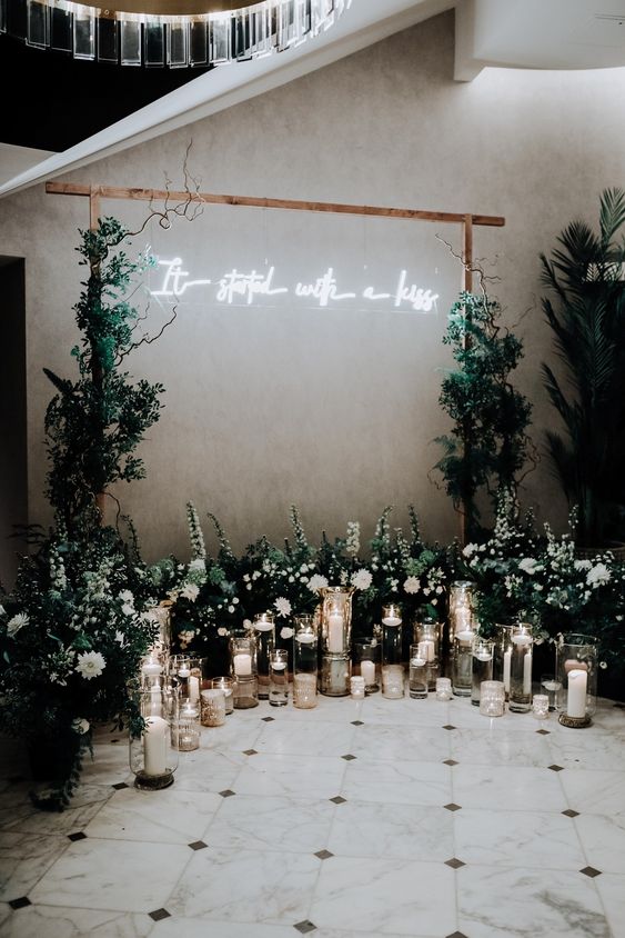 a modern wedding arch with greenery, twigs, a neon sign, a greenery and white bloom altar plus pillar candles is wow