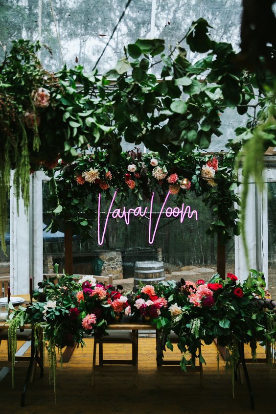 a modern wedding reception space with greenery, pink and neutral blooms and a pink neon sign is awesome