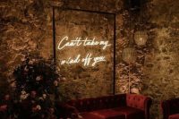 a moody wedding lounge with a burgundy sofa, bold blooms and greenery and a neon sign is amazing