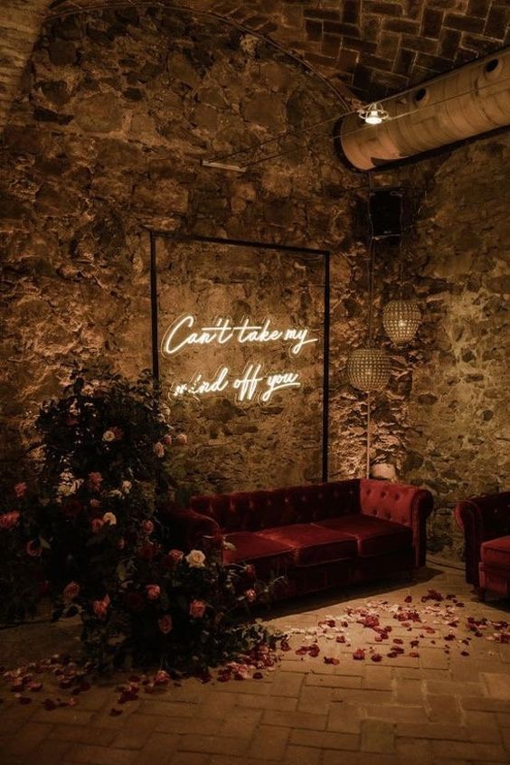 a moody wedding lounge with a burgundy sofa, bold blooms and greenery and a neon sign is amazing
