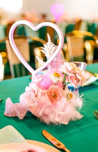 a pink wedding centerpiece of pink blooms, feathers, rocks, a neon heart sign is a cool and fun solution for a pink wedding