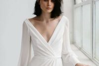 a simple minimalist wedding dress with a deep V-neckline, sleeves on buttons and a bit of drapery