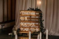 a simple wedding backdrop of a pallet with neon and greenery and candle lanterns is a lovely idea for a rustic space