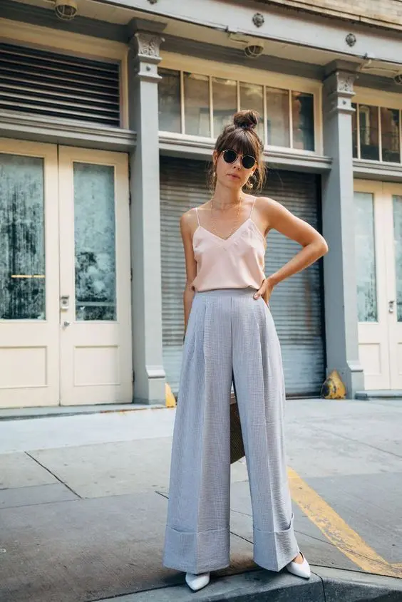 A summer wedding outfit with lavender colored wideleg pants, a blush spaghetti strap top, white shoes and statement earrings