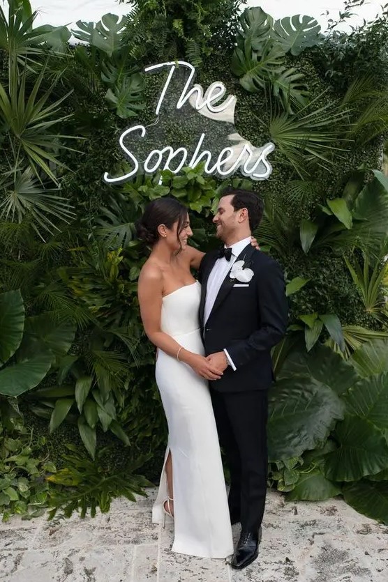 a super lush tropical foliage wall with a neon sign is a lovely idea for a modern or minimalist tropical wedding
