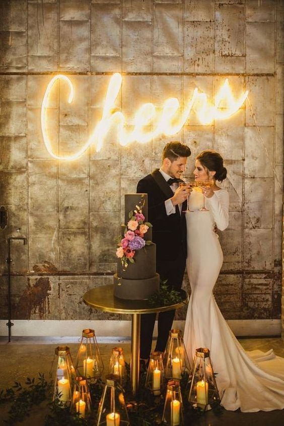 a wedding cake backdrop with a neon sign, a black cake with colored blooms and candle lanterns is wow