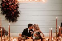a wedding sweetheart table with a lush ombre floral attangement and a neon sign and some candles on the table
