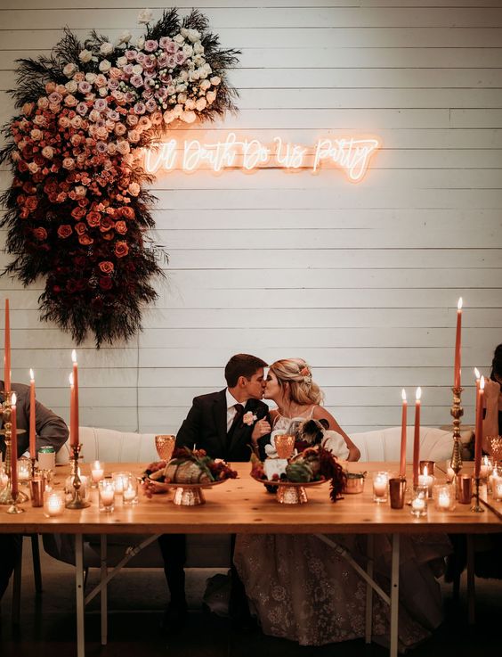 a wedding sweetheart table with a lush ombre floral attangement and a neon sign and some candles on the table