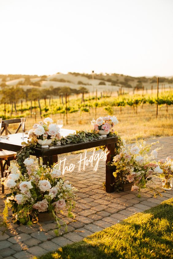 a wedding sweetheart table with white and blush blooms and greenery plus a neon sign is amazing