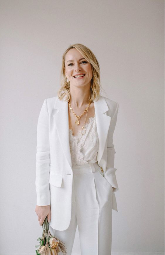 a white bridal pantsuit and a white lace top, layered necklaces and statement earrings for a very chic and elegant look