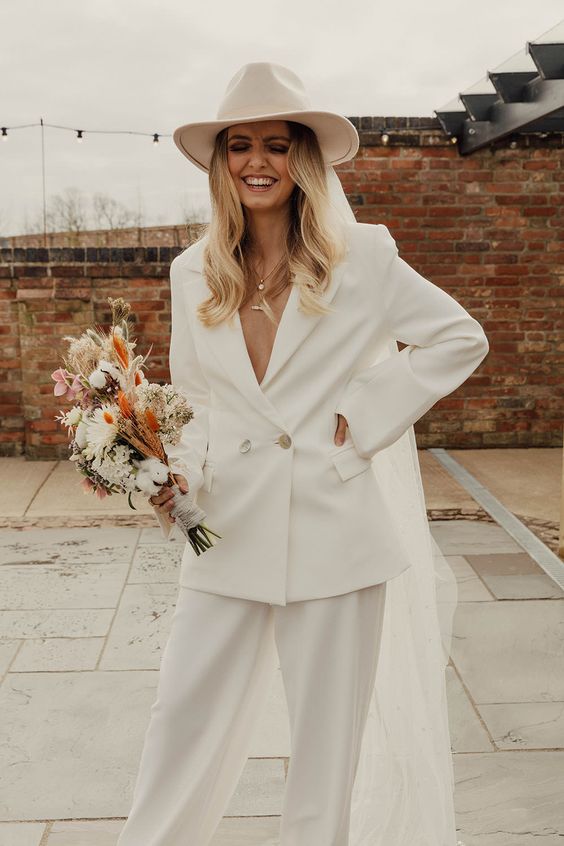 a white pantsuit with a deep neckline, a fedora hat with a veil for a more exquisite look and layered necklaces