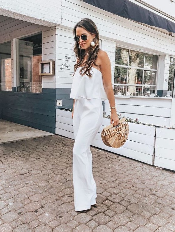 a white strapless jumpsuit with a tiered bodice, statement earrings and a wooden bag