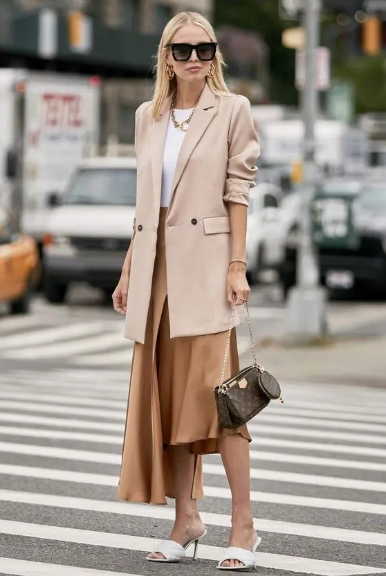 a white top, a chic asymmetrical skirt, white mules, a blush oversized blazer, statement accessories and a brown bag