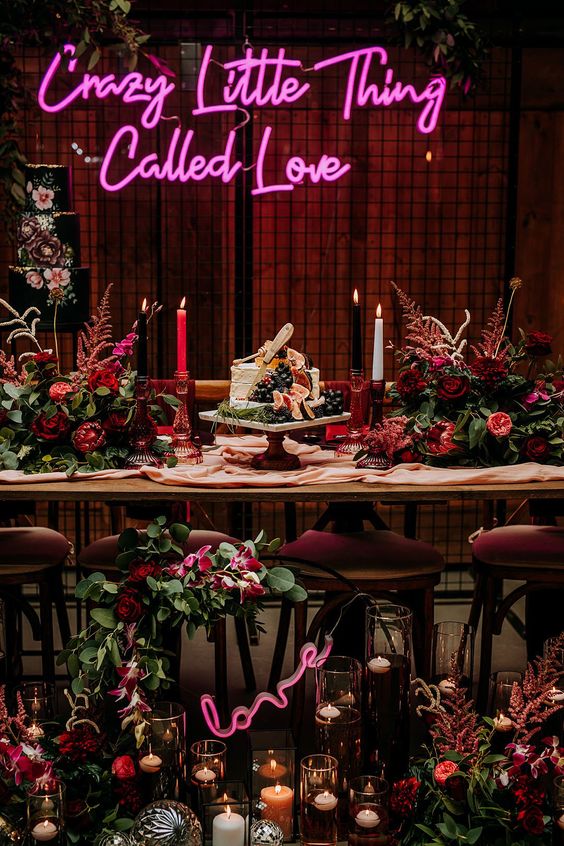 an extra bold wedding reception space with a pink neon sign, bold fuchsia and red blooms and greenery is wow
