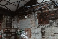 an industrial wedding space with shabby bricks, a metal arch with greenery and a neon sign, candles and floral arrangements
