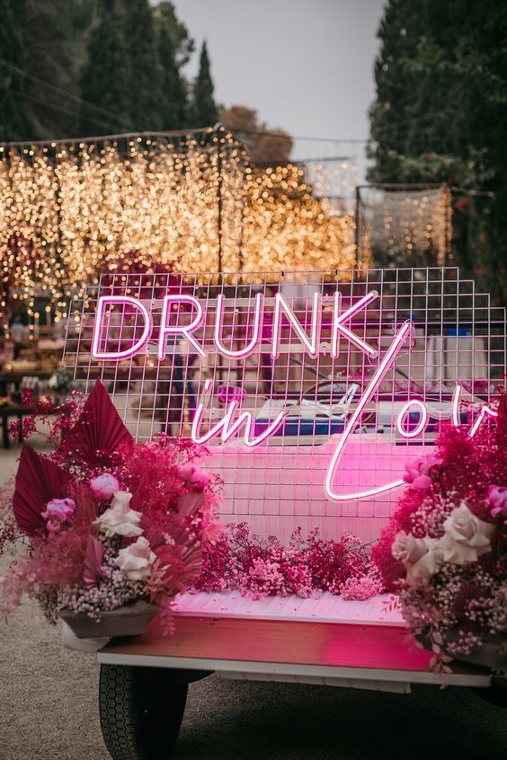 an outdoor wedding lounge with a pink seat, bold pink baby's breath and fronds and a pink neon sign in the backdrop