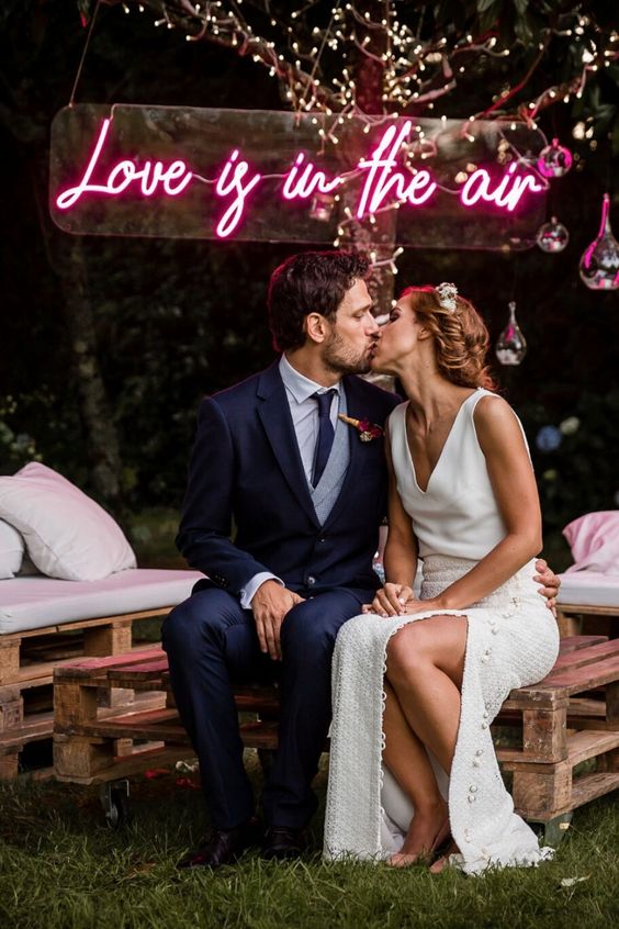 an outdoor wedding lounge with crate furniture, pillows, a pink neon sign over the head is a fun and cool idea