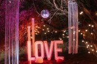 an outdoor wedding space with long fringe, colorful paper pieces, a disco ball, a large LOVE neon sign