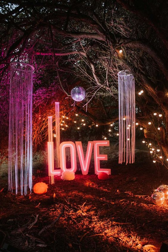an outdoor wedding space with long fringe, colorful paper pieces, a disco ball, a large LOVE neon sign