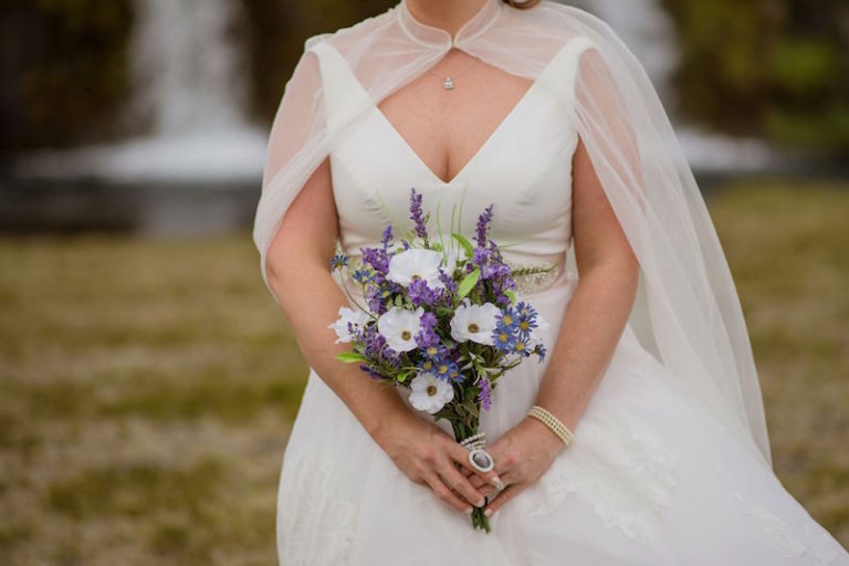 The bride was wearing an A line wedding dress with a deep neckline and a sheer cape plus some chic accessories