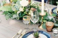 16 a chic and bright wedding tablescape with navy plates, a lush greenery and white bloom table runner, touches of gold