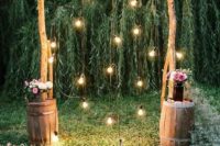 17 a rustic wedding arch of branches decorated with baby’s breath, with bulbs hanging down and some blooms in barrels