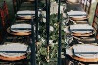 18 a navy and green tablescape with a lush runner, tall and thin candles, gold chargers and cutlery