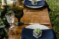 20 a relaxed wedding tablescape with pillar and tall candles, navy napkins, a eucalyptus table runner and blue and grey glasses