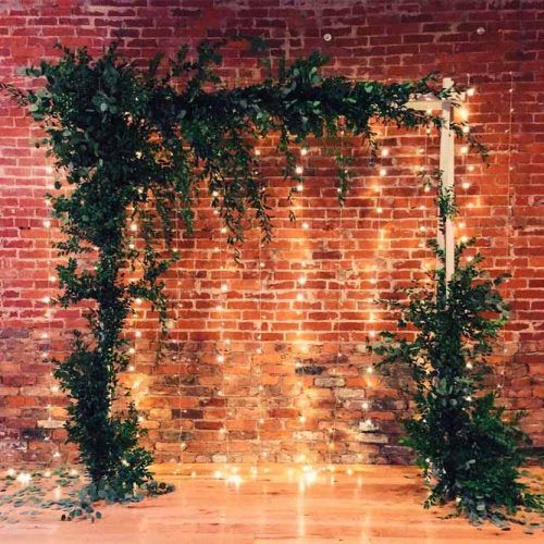 a simple indoor wedding arch decorated with lush greenery and with string lights that will highlight your couple