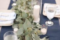 22 a simple and stylish reception table with a navy runner, a lush eucalyptus one, white candles and simple glasses