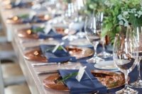 25 an elegant and bright wedding tablescape with lush greenery, a navy table runner and napkins and touches of copper