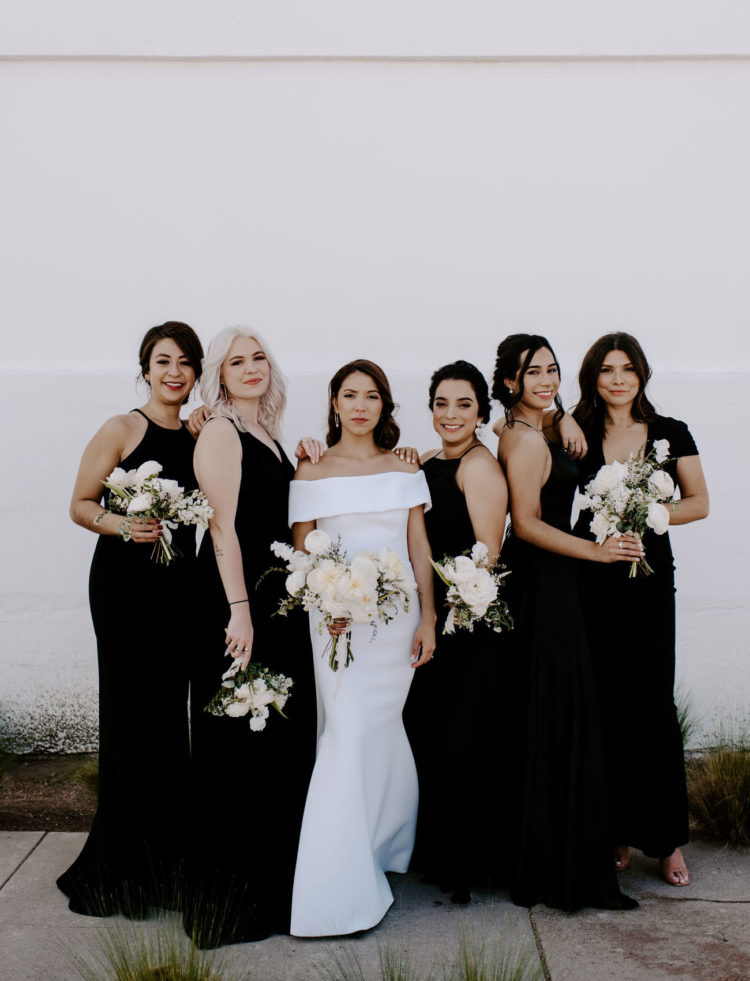 The bride was wearing an off the shoulder sheath wedding dress, the bridesmaids were rocking mismatching black gowns