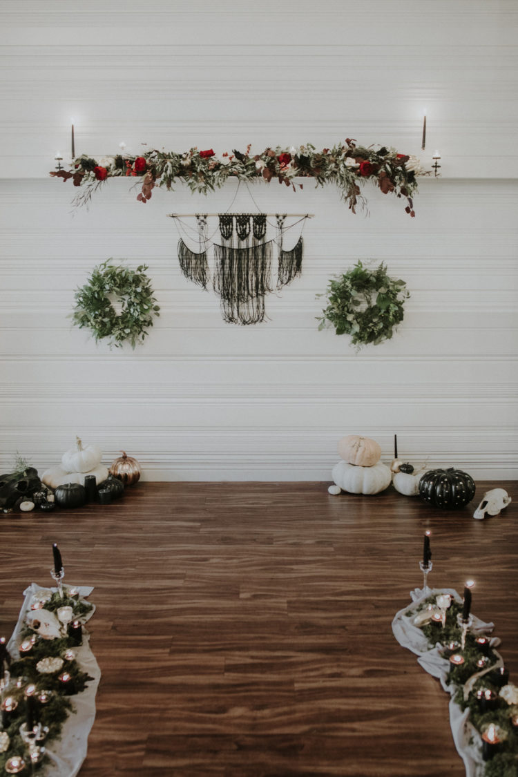 The wedding ceremony space was done with moody and white blooms, greenery, black macrame, greenery wreaths and pumpkins