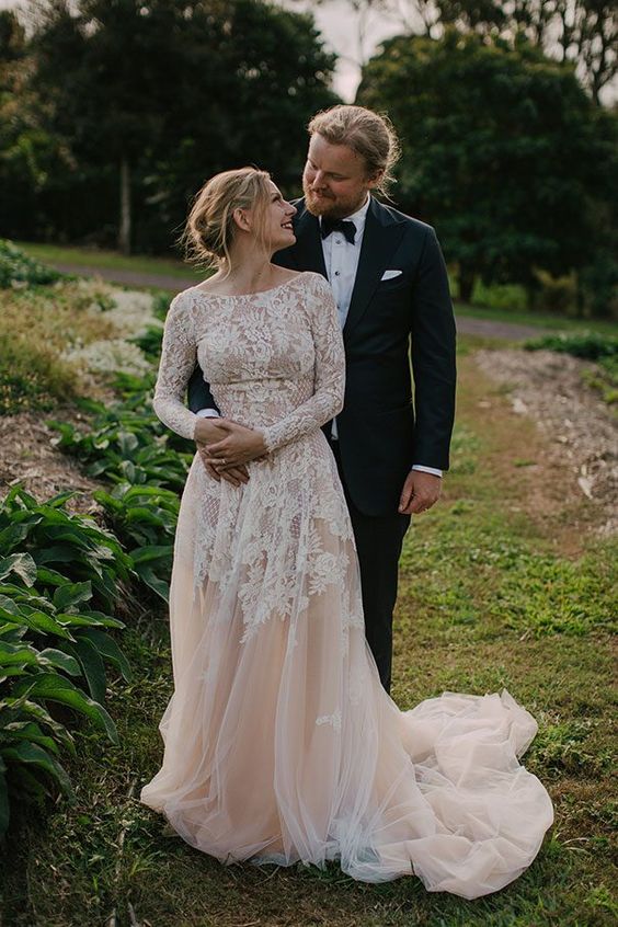 a blush A-line wedding dress with white lace with long sleeves, a high neckline and a train is very romantic